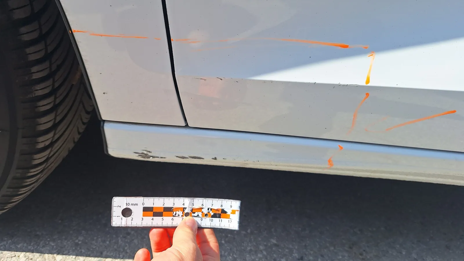 Zdjęcie SIXT z protokołu zwrotu: lewy próg z otarciami i lewe przednie drzwi z płytką rysą obrysowaną markerem, linijka dla skali