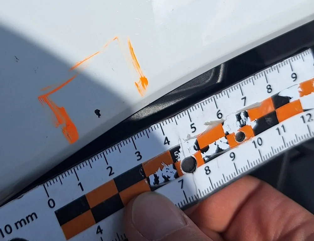Zdjęcie SIXT z protokołu zwrotu: pojedynczy odprysk lakieru około 2 mm na przednim zderzaku, obrysowany markerem, obok linijka milimetrowa